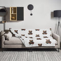 A white throw blanket featuring a repeating pattern of Boshino teddybear Bulldog illustrations, draped over a light gray sofa in a modern living room setting.